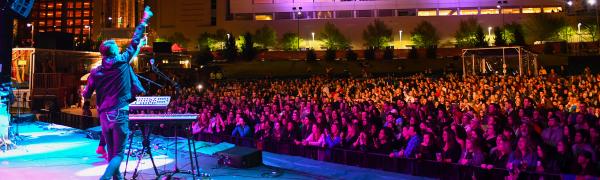A performer behind a keyboard points to the crowd during an evening show at Red Hat Amphitheater